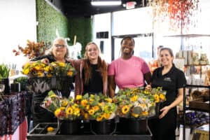 in bloom florist workers smiling in front of a bunch of flower bouquets for petal it forward