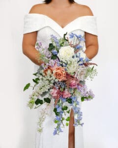 A cascading bridal bouquet with light blue delphiniums, white and peach roses, and other pastel flowers
