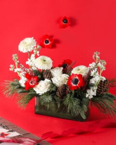 christmas centerpiece arrangement with red and white florals, pine cones, and holiday greenery